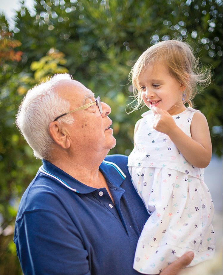 Grandfather holding his smiling granddaughter in the sunny outdoors