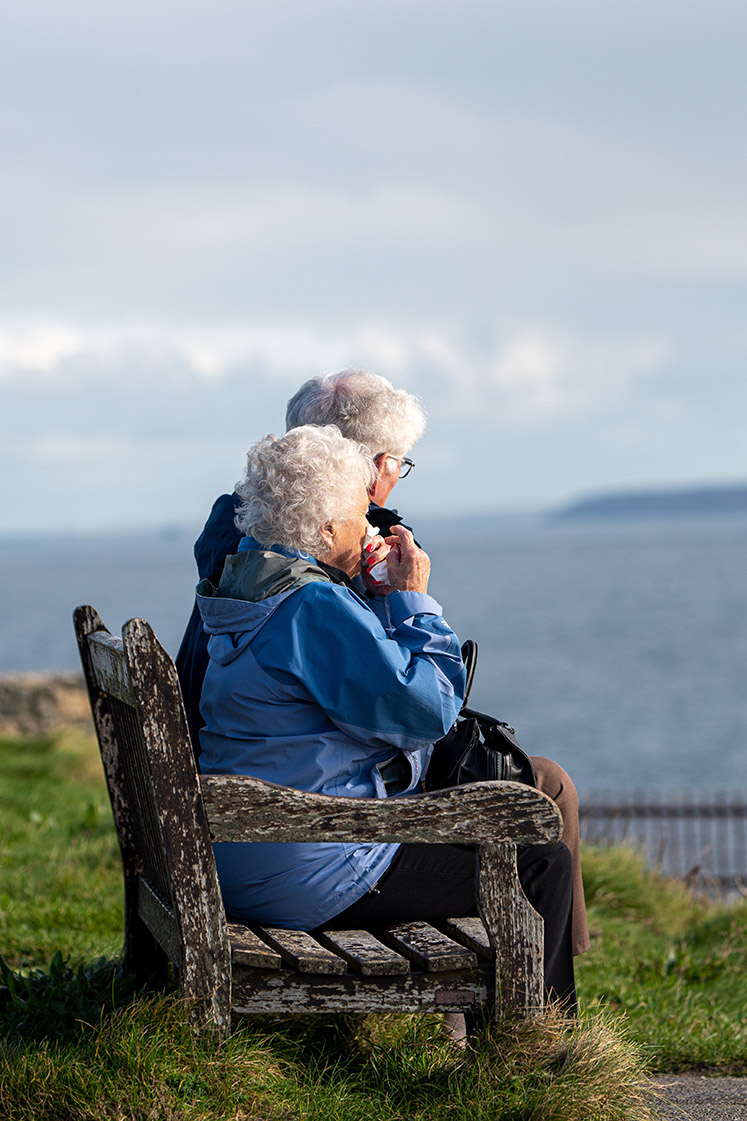 An elderly couple enjoying a sea view from a bench
